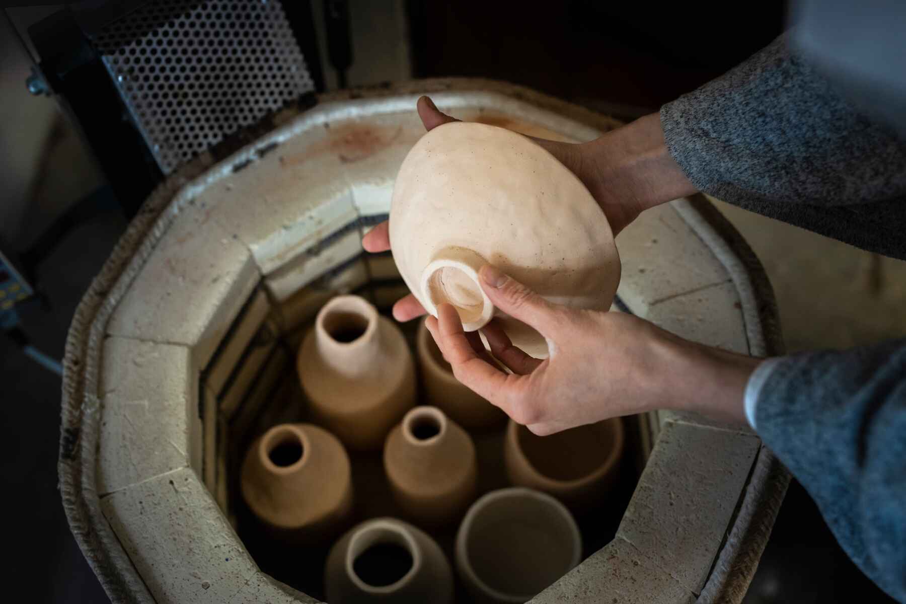 Person placing pottery bisqueware into an open electric round kiln