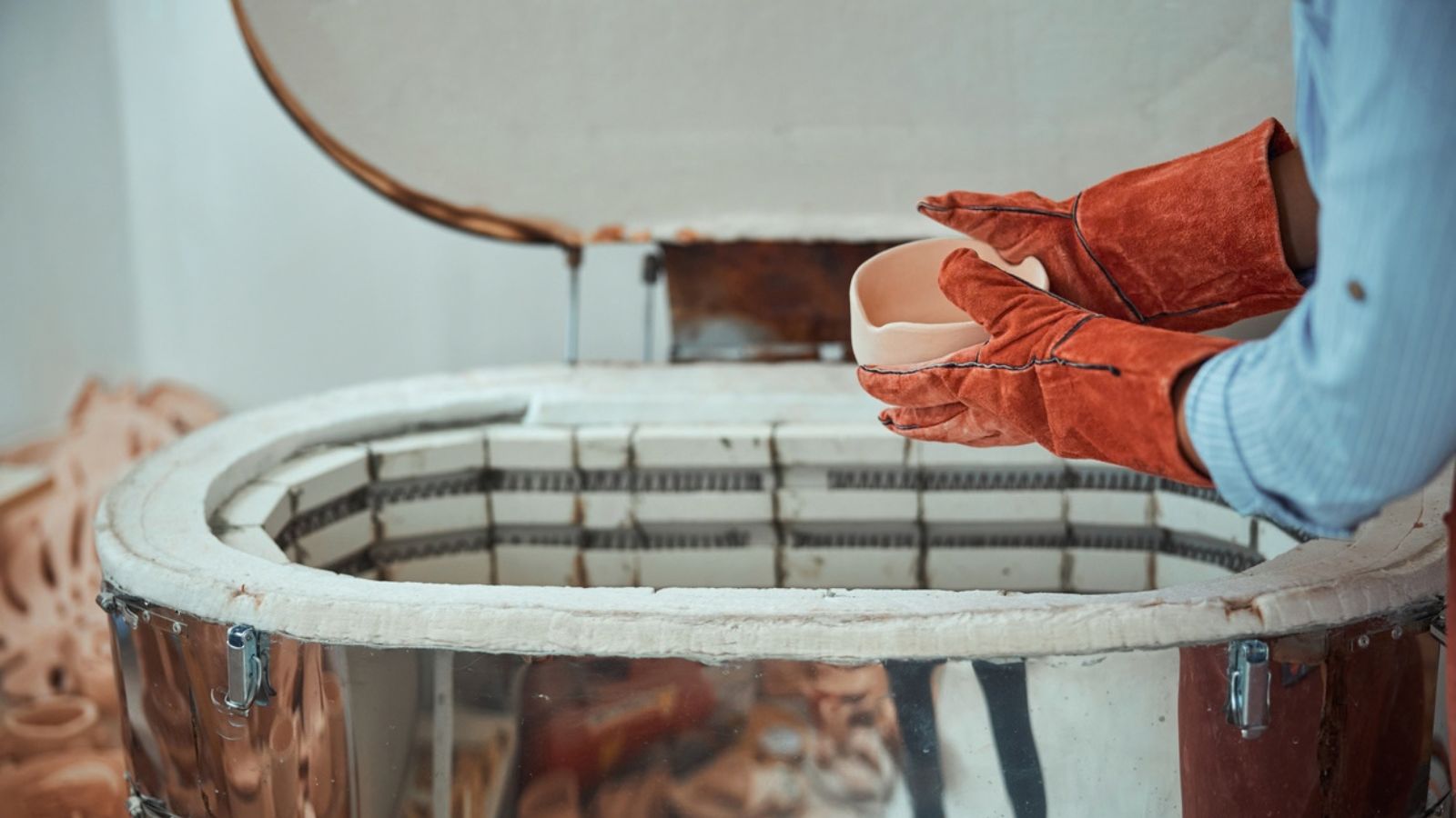 Person wearing heat-resistant gloves loading pottery into an electric kiln.