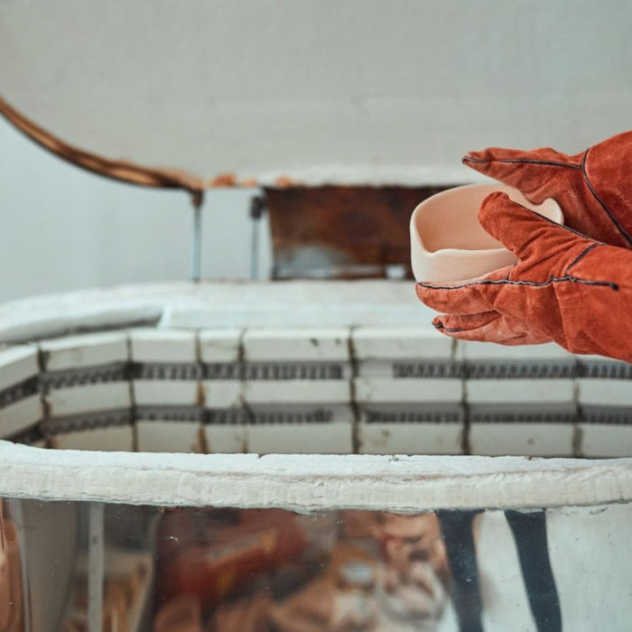 Person wearing heat-resistant gloves loading pottery into an electric kiln.