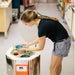 Woman in gray shorts - black shirt loading glazed ceramic pieces in to an open EMERGE ceramic-pottery kiln (model AF3C 15/13) from Jen-Ken  with the standard Orton AutoFire AF3C 3-Button Controller.
