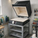 Clamshell lid opened on a Paragon Kilns CS26 glass fusing kiln placed on a stand in a workshop.